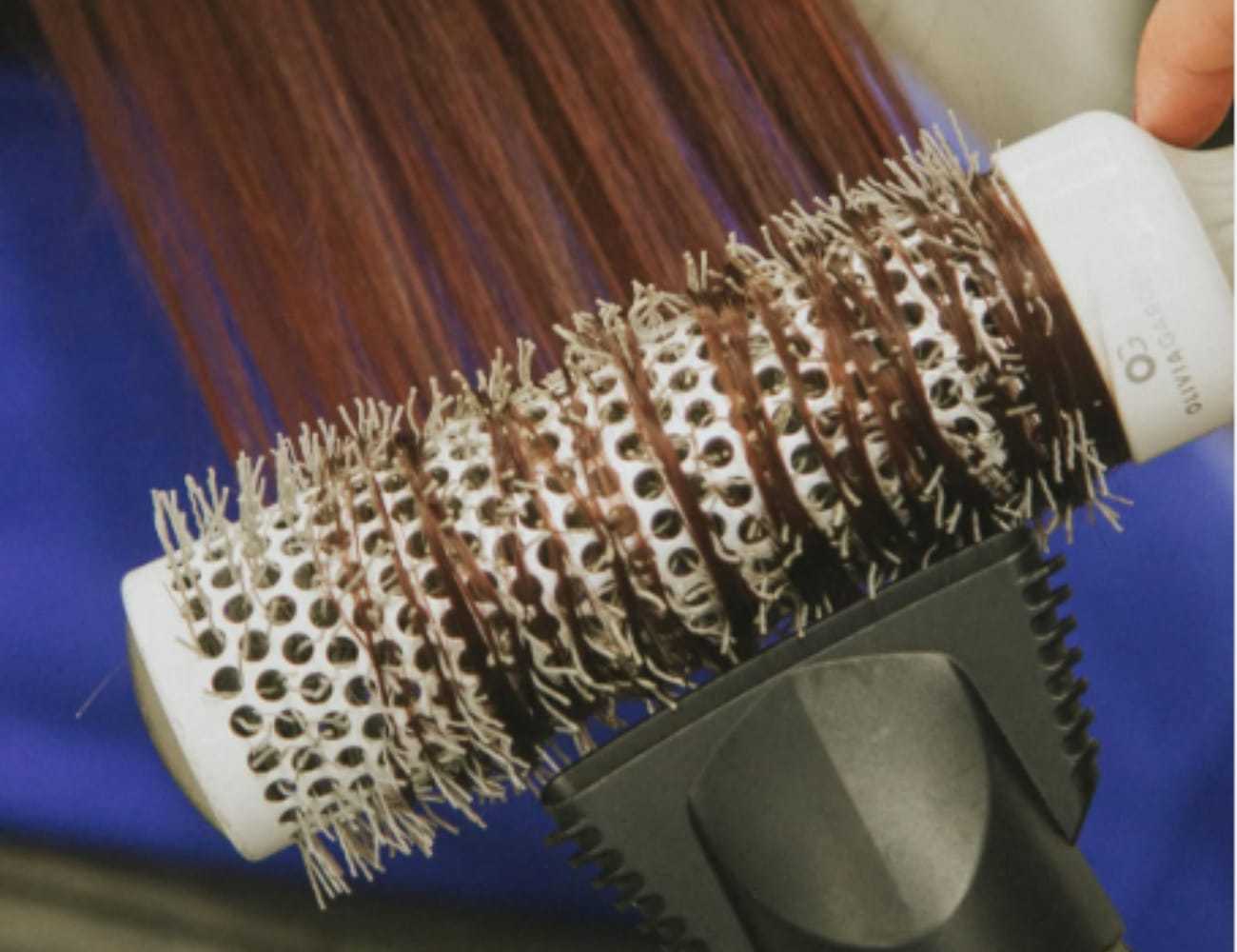 Hairbrush with metal bristles and brown hair being combed through.