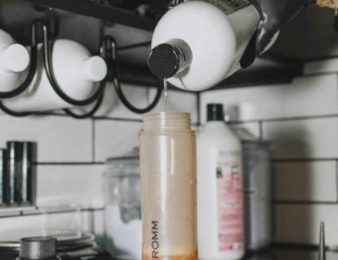 Refilling a reusable bottle with shampoo dispenser in tiled bathroom.